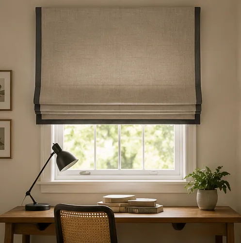 A natural linen Roman blind edged with a dark charcoal border, above a desk